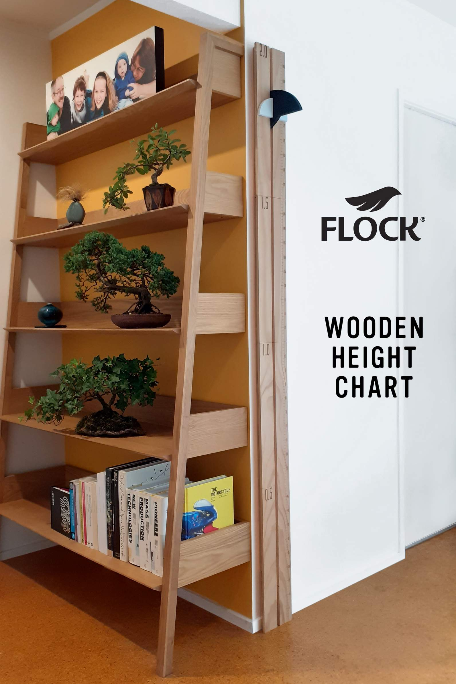 A FLOCK height chart is displayed on a wall corner by a shelf of bonsai trees, art and design books.